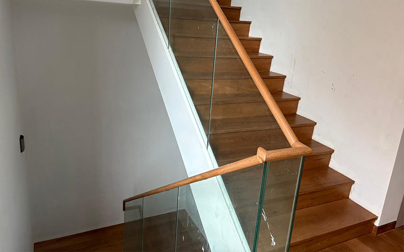 A modern staircase featuring a sleek wooden handrail paired with glass panels